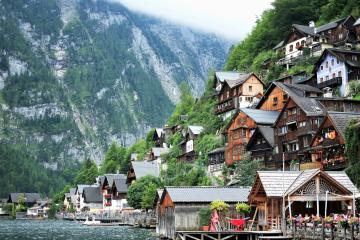 A scenic view of the village of Hallstatt, Austria, showing traditional wooden houses built on a steep hillside overlooking Lake Hallstatt, with mountains in the background and a pier in the foreground.