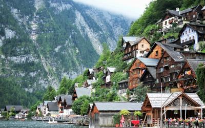 A scenic view of the village of Hallstatt, Austria, showing traditional wooden houses built on a steep hillside overlooking Lake Hallstatt, with mountains in the background and a pier in the foreground.