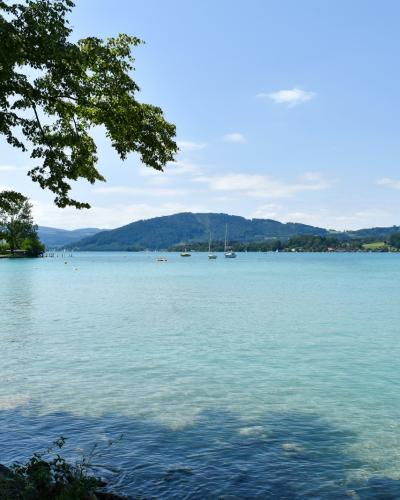 Calm turquoise Austrian lake with sailboats and low wooded hills under a summer sky
