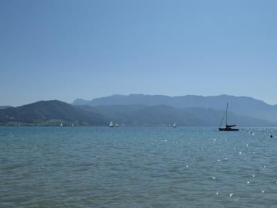 Sailboats on a broad turquoise lake beneath a mountain ridge, seen from the shoreline