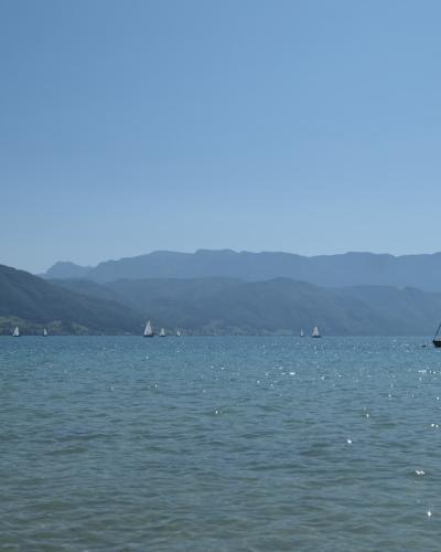 Sailboats on a broad turquoise lake beneath a mountain ridge, seen from the shoreline