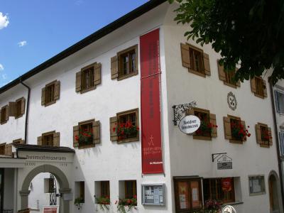 A white, multi-story building with brown wooden shutters and flower boxes, featuring a hanging sign that reads "Montafoner Heimatmuseum" and an entrance archway labeled "heimatmuseum" with the year "1978".