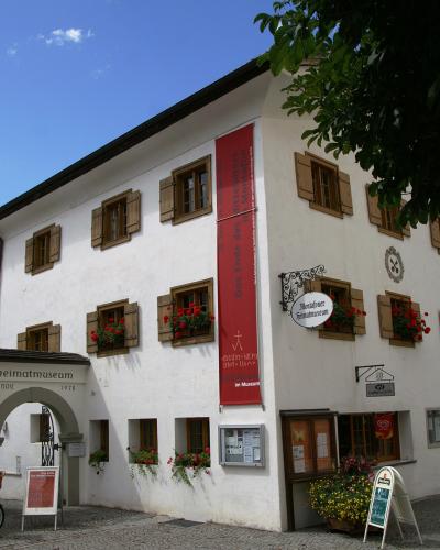 A white, multi-story building with brown wooden shutters and flower boxes, featuring a hanging sign that reads "Montafoner Heimatmuseum" and an entrance archway labeled "heimatmuseum" with the year "1978".