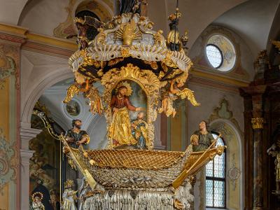An ornate Baroque pulpit inside a church, featuring a boat-shaped sounding board with a net, a central painting of Jesus, and a column topped by a statue of Christ.