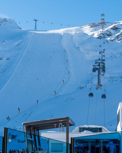 A snowy mountain ski slope with chairlifts and a modern station building in the foreground, featuring a vertical sign reading "SCHWARZE SCHNEIDE".