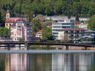 A scenic view of the Hotel Astoria and the yellow church tower of St. John the Baptist Church rising behind it, situated on the shore of Lake Wörthersee in Pörtschach, Austria.
