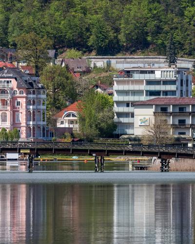 A scenic view of the Hotel Astoria and the yellow church tower of St. John the Baptist Church rising behind it, situated on the shore of Lake Wörthersee in Pörtschach, Austria.