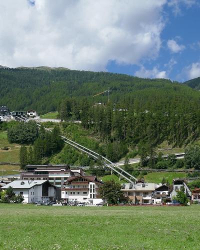 A wide landscape shot of the village of Sölden in the Ötztal Alps, showing traditional alpine buildings in the foreground and a cable car line ascending the forested mountain slope towards the Rettenbach glacier area.