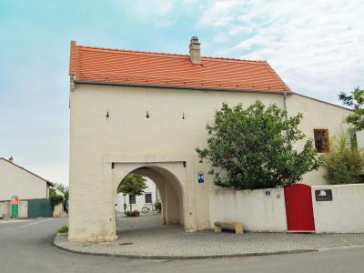 A white, two-story building with a red tiled roof, featuring a large arched passageway on the ground floor, a red gate to the right, and a blue and white sign on the wall.