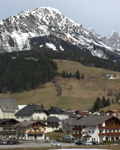 A view of the village of Filzmoos in the Salzburg region of Austria, featuring the white parish church with a green spire in the foreground and snow-capped mountains in the background.