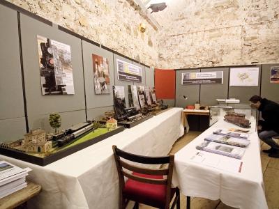 An indoor exhibition space with model trains and informational posters on grey partition walls, featuring a person examining a display case.