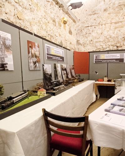 An indoor exhibition space with model trains and informational posters on grey partition walls, featuring a person examining a display case.