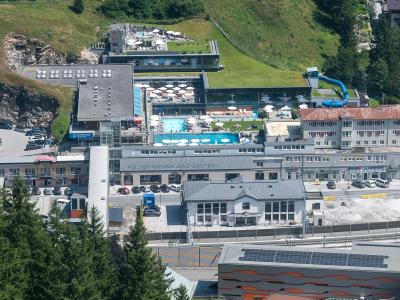 An aerial view of a large thermal bath complex built into a hillside, featuring multiple outdoor pools, a blue water slide, and surrounding parking areas.
