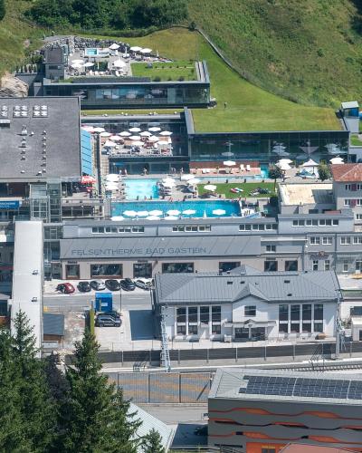 An aerial view of a large thermal bath complex built into a hillside, featuring multiple outdoor pools, a blue water slide, and surrounding parking areas.