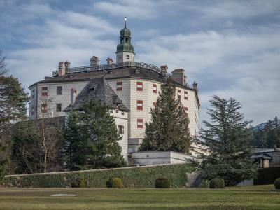 A large, white Renaissance-style castle with a prominent central tower, green copper roof, and distinctive red-and-white window shutters, viewed from a grassy lawn with trees and hedges in the foreground.