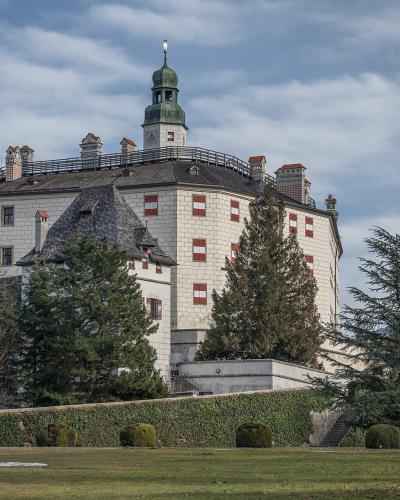 A large, white Renaissance-style castle with a prominent central tower, green copper roof, and distinctive red-and-white window shutters, viewed from a grassy lawn with trees and hedges in the foreground.