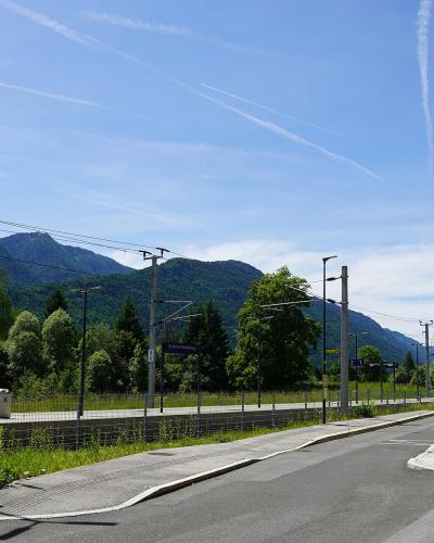 A view of a railway station platform and adjacent road with mountains in the background, featuring a purple station sign reading "St. Stefan-Vorderberg" and a "P+R" parking sign.