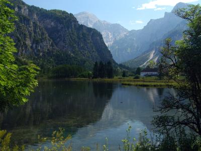 A scenic view of a calm alpine lake surrounded by steep, forested mountains and a white building on the far shore.
