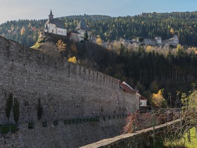 A view of a massive stone retaining wall in the foreground with the Petersberg hill, featuring the Peterskirche and castle ruins, rising in the background.