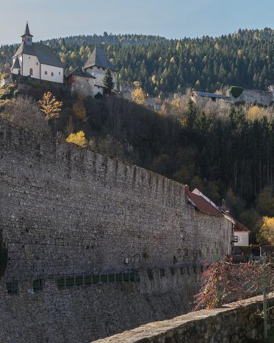 A view of a massive stone retaining wall in the foreground with the Petersberg hill, featuring the Peterskirche and castle ruins, rising in the background.