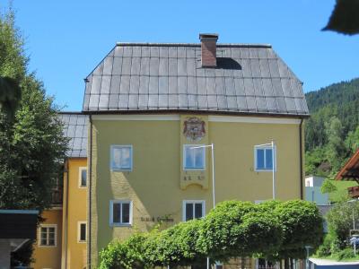 A yellow building with a dark roof, featuring a coat of arms and the text "Schloß Lerchen" on its facade, set against a backdrop of green trees and a blue sky.