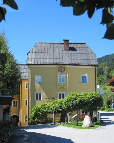 A yellow building with a dark roof, featuring a coat of arms and the text "Schloß Lerchen" on its facade, set against a backdrop of green trees and a blue sky.