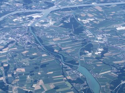 An aerial photograph showing a wide, braided river system flowing through a patchwork of agricultural fields and small settlements, with a larger body of water visible in the upper portion.