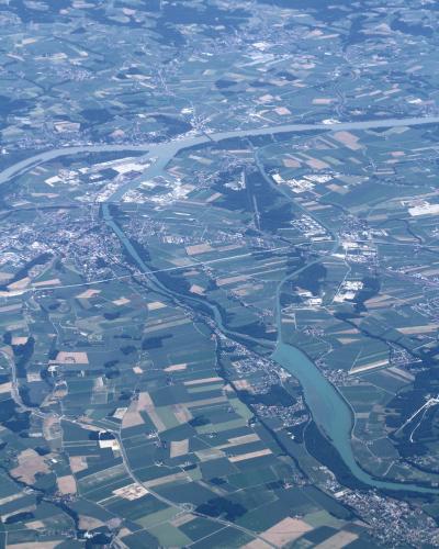 An aerial photograph showing a wide, braided river system flowing through a patchwork of agricultural fields and small settlements, with a larger body of water visible in the upper portion.