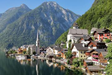 A scenic view of the lakeside village of Hallstatt, Austria, featuring its iconic church spire, traditional alpine houses, and the Salzkammergut lake with mountains in the background.
