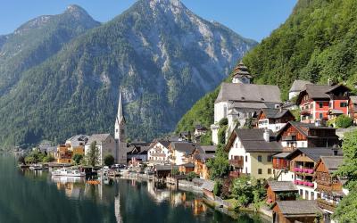 A scenic view of the lakeside village of Hallstatt, Austria, featuring its iconic church spire, traditional alpine houses, and the Salzkammergut lake with mountains in the background.