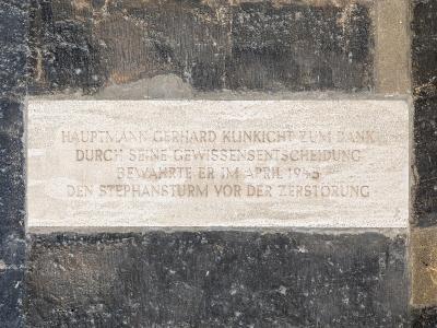 A close-up of a commemorative plaque mounted on a dark stone wall, inscribed with German text honoring Hauptmann Gerhard Klinkicht for saving the "Stephansturm" (St. Stephen's Tower) from destruction in April 1945.