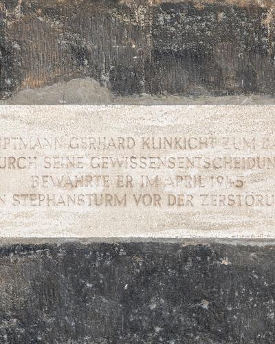 A close-up of a commemorative plaque mounted on a dark stone wall, inscribed with German text honoring Hauptmann Gerhard Klinkicht for saving the "Stephansturm" (St. Stephen's Tower) from destruction in April 1945.