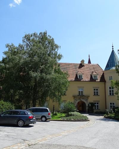 A yellow Renaissance-style castle with two conical-roofed towers and a central arched entrance, viewed from a paved driveway with parked cars under a blue sky.