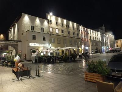 A night view of a town square showing a large, illuminated historic building with an outdoor cafe seating area and a sign reading "SCHLOSSMUSEUM" above an archway.