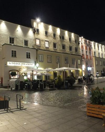 A night view of a town square showing a large, illuminated historic building with an outdoor cafe seating area and a sign reading "SCHLOSSMUSEUM" above an archway.