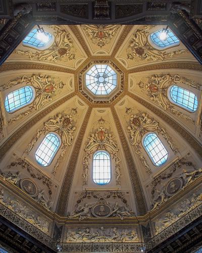 An ornate, octagonal dome ceiling with gilded stucco decorations, frescoes, and multiple arched windows, viewed from below.