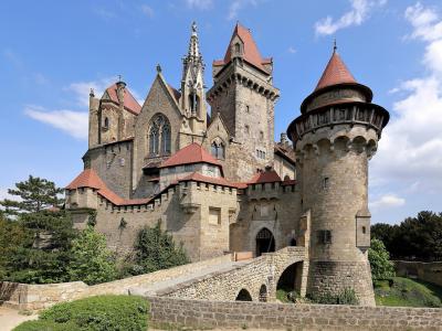 Burg Kreuzenstein's towers, battlements and stone bridge under a blue sky in Leobendorf