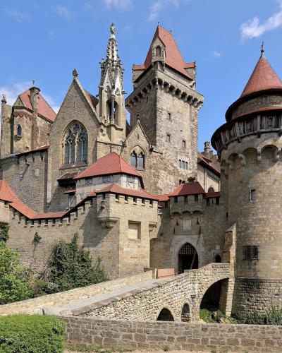 Burg Kreuzenstein's towers, battlements and stone bridge under a blue sky in Leobendorf