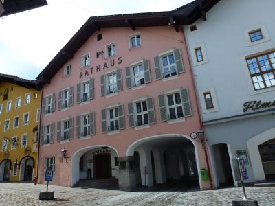 A low-angle shot of a pink building with grey shutters and the word "RATHAUS" displayed prominently on the facade and above the entrance archway, situated in a cobblestone square.