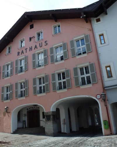 A low-angle shot of a pink building with grey shutters and the word "RATHAUS" displayed prominently on the facade and above the entrance archway, situated in a cobblestone square.