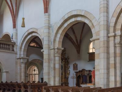 The interior nave of a historic church showing stone arcades, wooden pews, and a side chapel area with religious statuary.