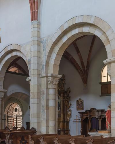The interior nave of a historic church showing stone arcades, wooden pews, and a side chapel area with religious statuary.