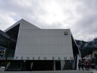 The image shows the modern, angular facade of a cable car station building with large lettering reading "PENKENBAHN" across the front and a logo for "Mayrhofen" on the upper right side.