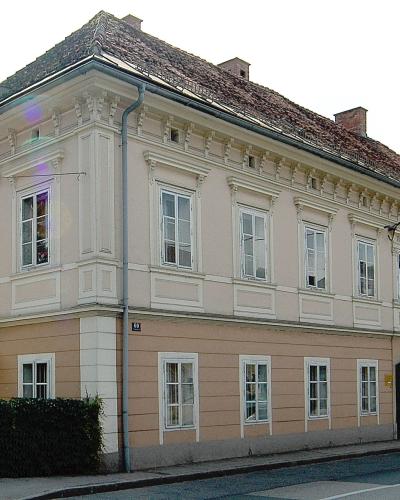 A two-story, cream-colored building with a tiled roof and white window frames, featuring a street number plaque reading "69" on the corner.