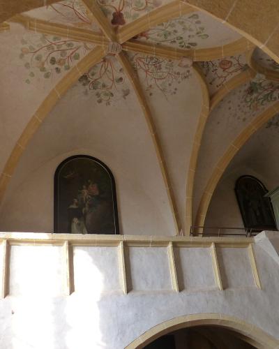 The image shows the interior of a church featuring a gallery with vaulted ceilings decorated with floral motifs, religious paintings, and a small organ.