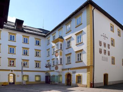 A white and yellow historic building with a courtyard, featuring a coat of arms and text on the wall, identified by the filename as 'Museum Kitzbühel, Hinterstadt 32'.