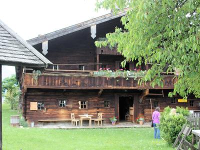 A traditional wooden Alpine farmhouse with a balcony, flower boxes, and outdoor seating, with a person standing near the entrance.