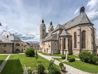 A large stone church with two onion-domed towers and an adjacent octagonal ossuary (charnel house) set within a grassy courtyard under a cloudy sky.