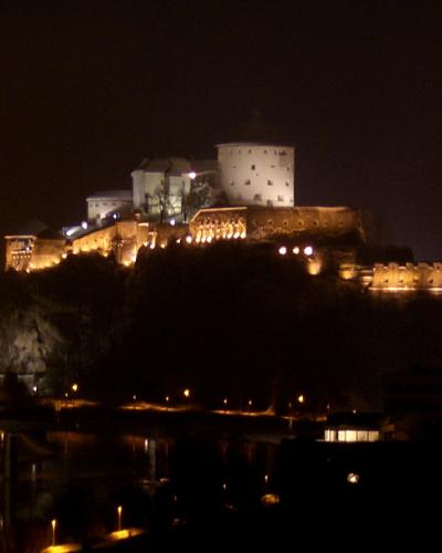 A night photograph of a large, illuminated fortress complex situated on a rocky hill overlooking a river and a town with streetlights.