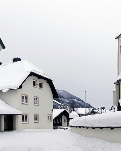 A view of a white-walled church building with a slate roof, a cemetery wall in the foreground, a wooden crucifix, and a distinctive jagged mountain peak in the background.